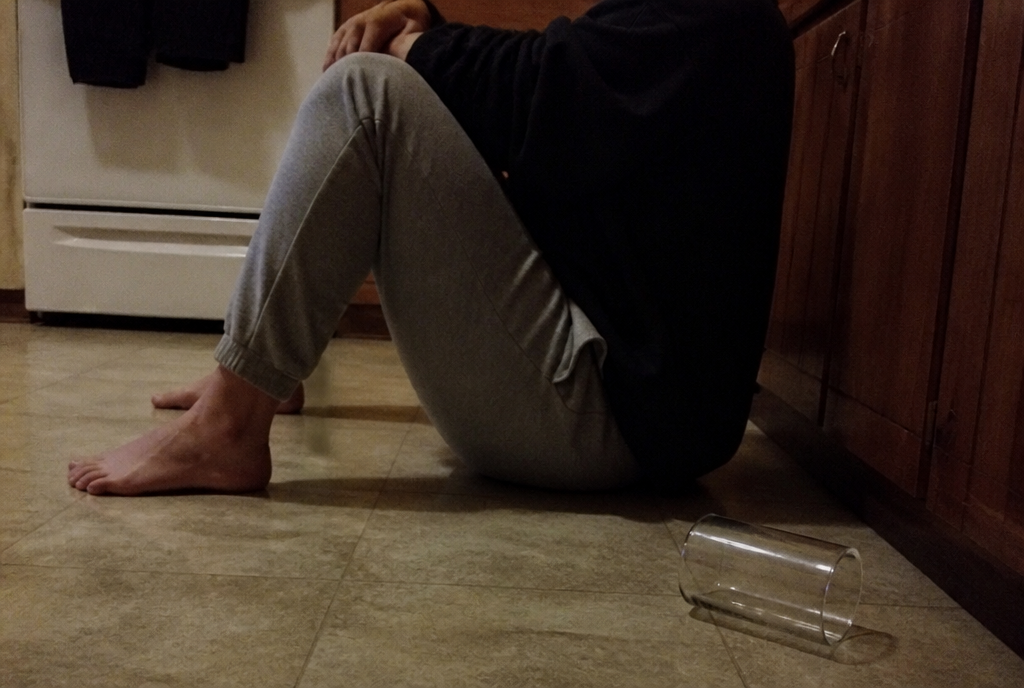 A person sitting on a kitchen floor against the cabinets